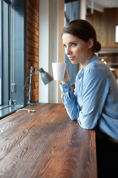 Young attractive girl  sitting alone near big window in coffee shop during free time and working  - Zdjęcie, obraz