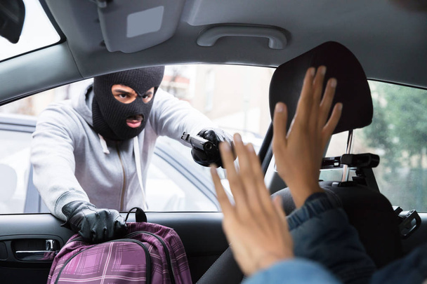 Thief In Balaclava Threatening Woman With Gun While Stealing Backpack From Car - Foto, imagen