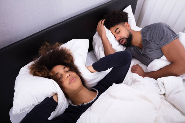 Elevated View Of Young Woman Covering Her Ears With Pillow While Man Snoring In Bed - Photo, image