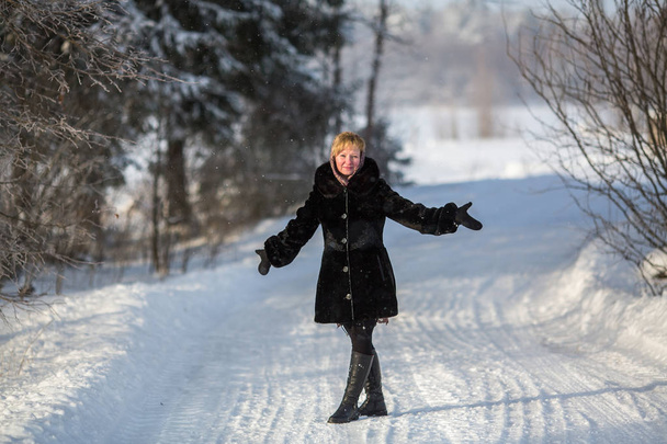 Mladá žena hodí se mu ruce, stojící na cestě v zimě na zasněženém parku. - Fotografie, Obrázek