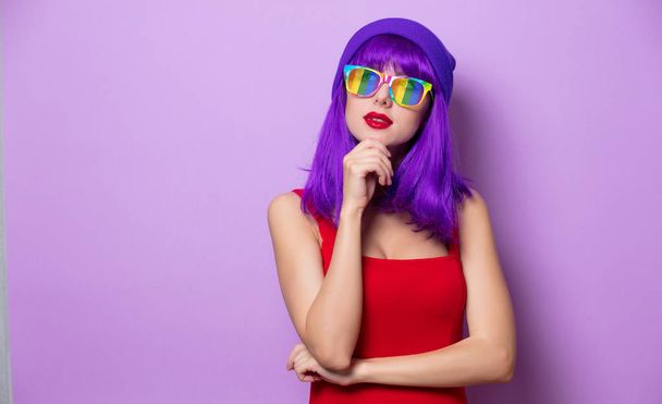ピンクの背景に紫の髪と虹の眼鏡と若いスタイルの流行に敏感な女の子の肖像画 - 写真・画像