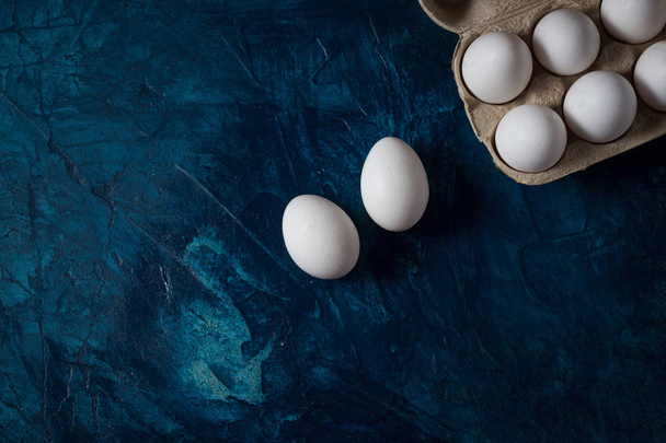 White Eggs in an open cardboard box on a blue background and a f - Fotografie, Obrázek