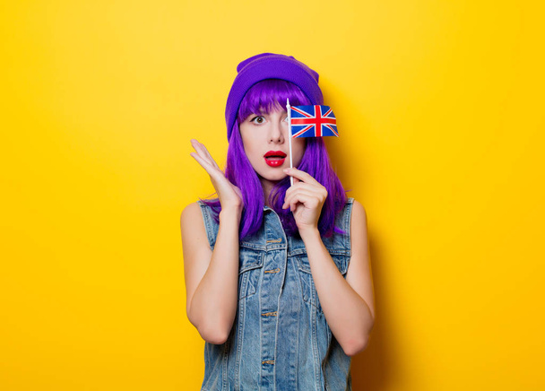 Portrét mladé styl bederní dívka s fialovými vlasy a Velké Británie vlajka v ruce na žlutém podkladu - Fotografie, Obrázek