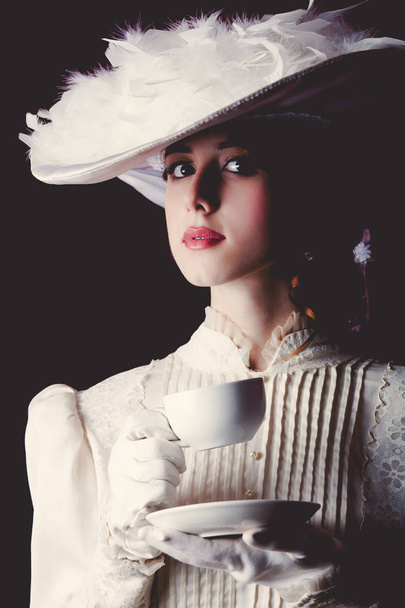 Young redhead woman in white Victorian era clothes with cup of tea on black background. - Photo, Image