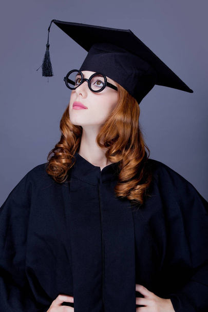 Jeune fille diplômée rousse en chapeau académique carré et manteau sur fond gris
 - Photo, image