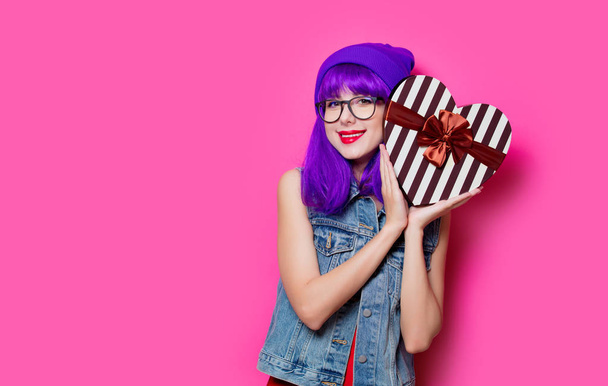 Retrato de chica hipster de estilo joven con peinado púrpura con caja de regalo de San Valentín sobre fondo rosa
 - Foto, Imagen