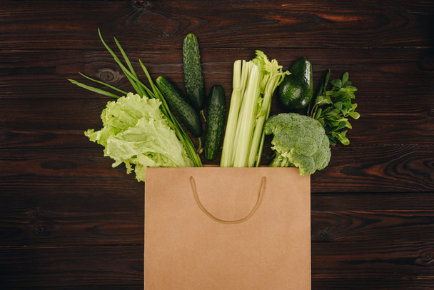 top view of green vegetables in shopping bag on wooden table - Photo, Image