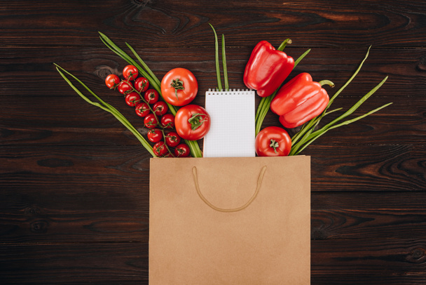 top view of red tomatoes and bell peppers with empty notebook on wooden table, grocery concept - Фото, зображення