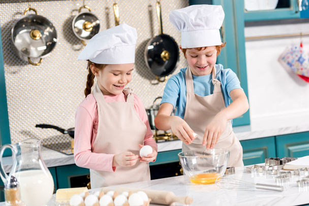 cute smiling kids in chef hats and aprons preparing dough together in kitchen - Foto, immagini