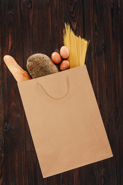 top view of bread, pasta and eggs in shopping bag on wooden table, grocery concept - 写真・画像