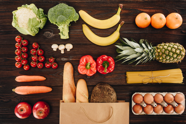 bovenaanzicht van groenten en fruit, brood en eieren op houten tafel, kruidenier concept - Foto, afbeelding