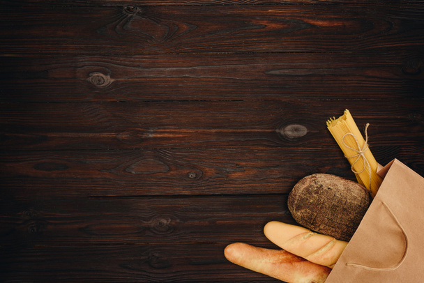 pohled shora chleba a těstoviny v nákupní tašce na dřevěný stůl, koncept s potravinami - Fotografie, Obrázek
