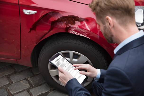 Man Looking At Digital Tablet Screen Showing Insurance Claim Form Near Car - Foto, afbeelding