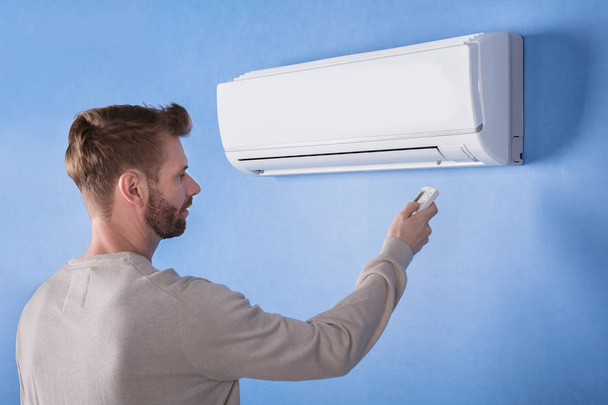 Rear View Of A Young Man Operating Air Conditioner Mounted On Blue Wall - Foto, Imagem