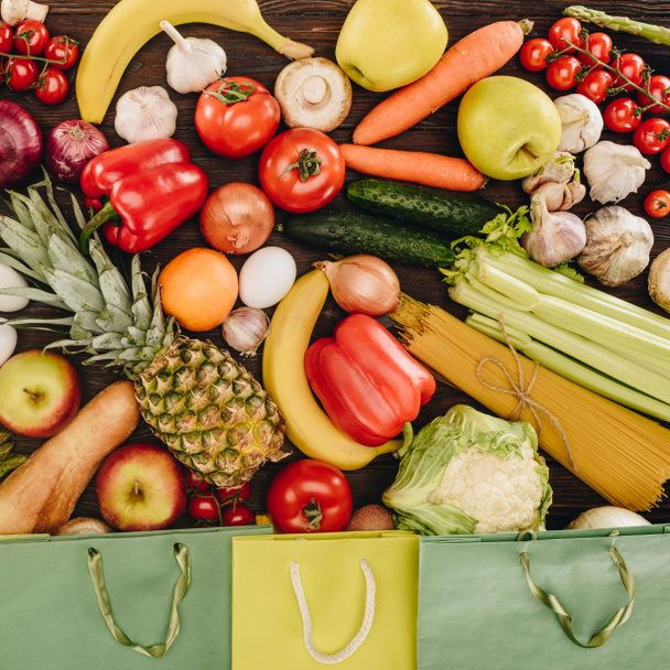 top view of vegetables with fruits and shopping bags on wooden table, grocery concept - Photo, Image