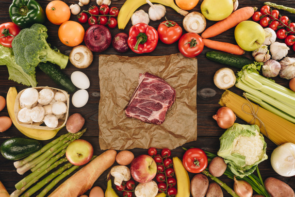 Blick von oben auf rohes Fleisch zwischen Gemüse und Obst auf Holztisch - Foto, Bild