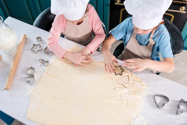 bovenaanzicht van kinderen in chef-kok hoeden cookies samen voorbereiden - Foto, afbeelding