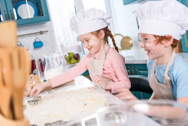 happy little children in chef hats preparing cookies together in kitchen - Foto, afbeelding