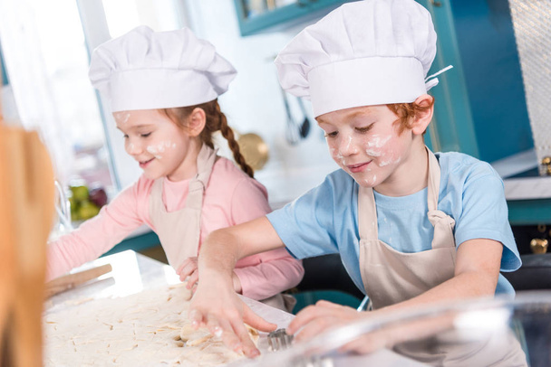 śliczne małe dzieci w kapeluszach szef kuchni przygotowuje ciasteczka razem - Zdjęcie, obraz