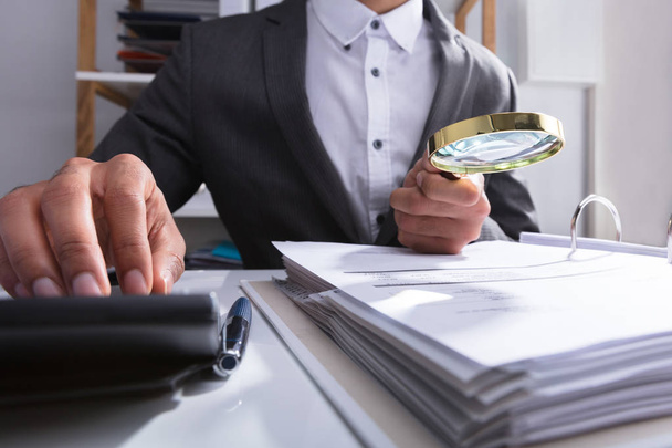 Businessperson's Hand Analyzing Bill With Magnifying Glass At Workplace - Photo, Image