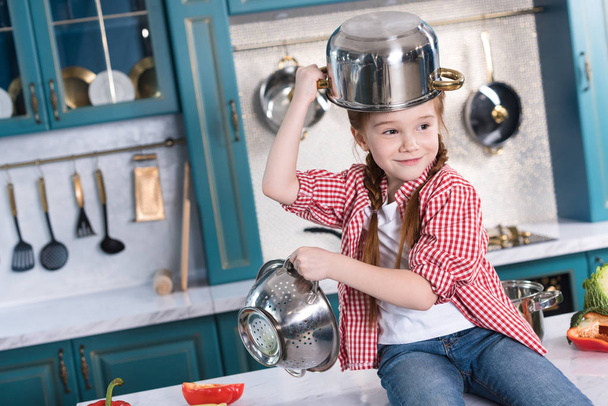 roztomilé malé dítě baví s nádobím při posezení na kuchyňském stole - Fotografie, Obrázek