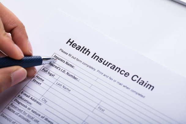 Close-up Of A Human Hand Filling Health Insurance Claim Form With Pen - Foto, Bild