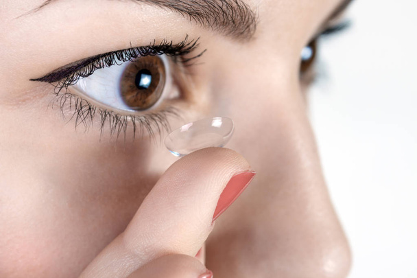 Молодая женщина кладет контактные линзы в правый глаз, закрыть
 - Фото, изображение