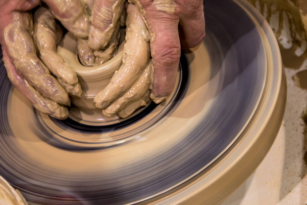 aardewerk maken van een pot van ruwe klei op een Potters machine met mannen handen leren. De oude mode ambachtelijke aardewerk - Foto, afbeelding