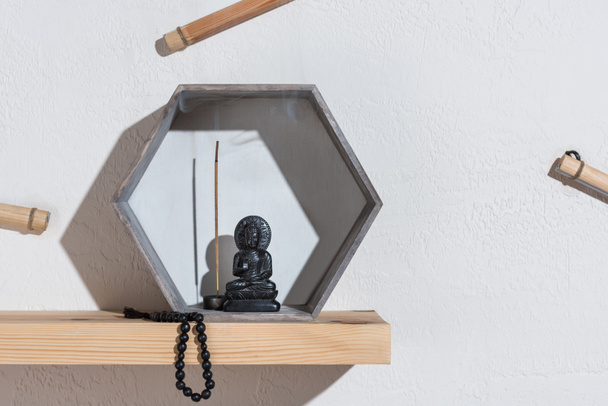 klein standbeeld van Boeddha in frame en rozenkrans op houten plank - Foto, afbeelding