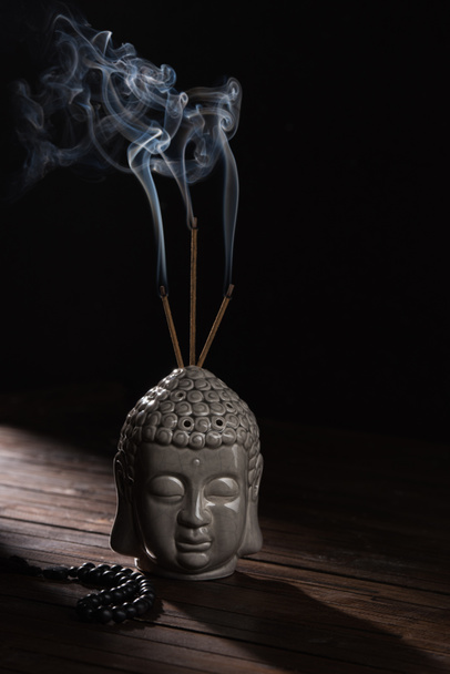 sculpture of buddha head with burning incense sticks - Photo, Image
