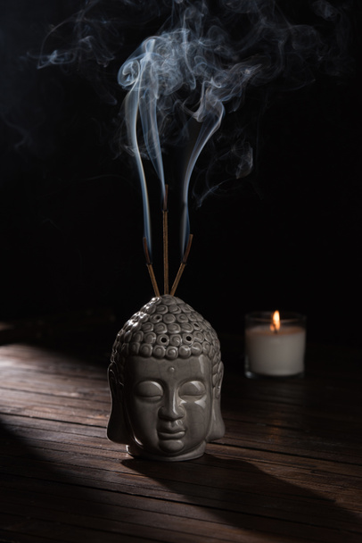 sculpture of buddha head with burning incense sticks and candle on table - Photo, Image