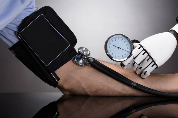 Robotova ruka kontrola osoby krevní tlak na šedém pozadí - Fotografie, Obrázek