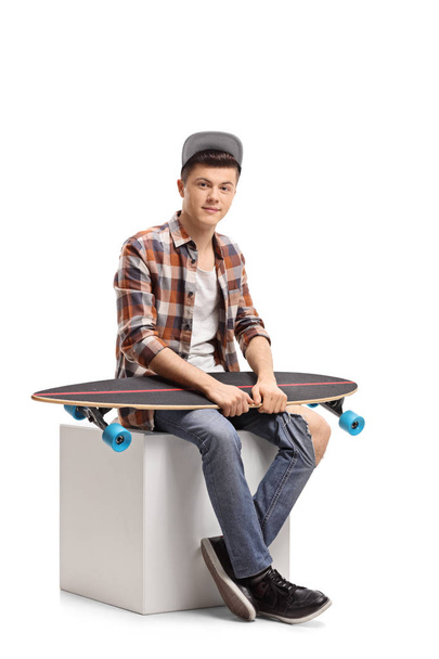 Teenage hipster with a longboard sitting on a cube isolated on white background - Φωτογραφία, εικόνα