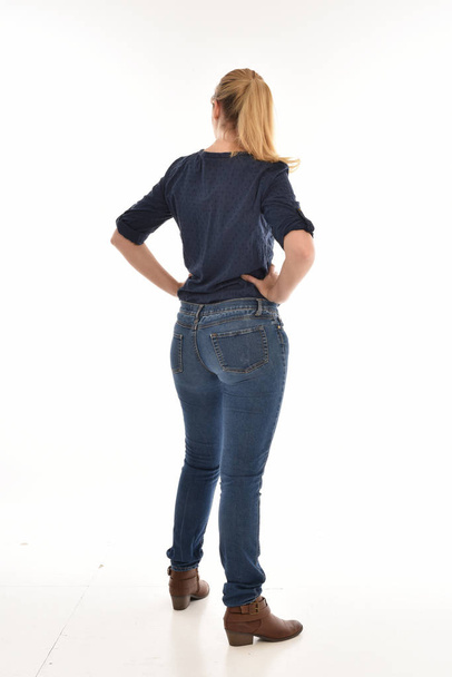 retrato de longitud completa de chica rubia con camisa azul simple y pantalones vaqueros, de pie pose frente a la cámara. aislado sobre fondo blanco
. - Foto, Imagen