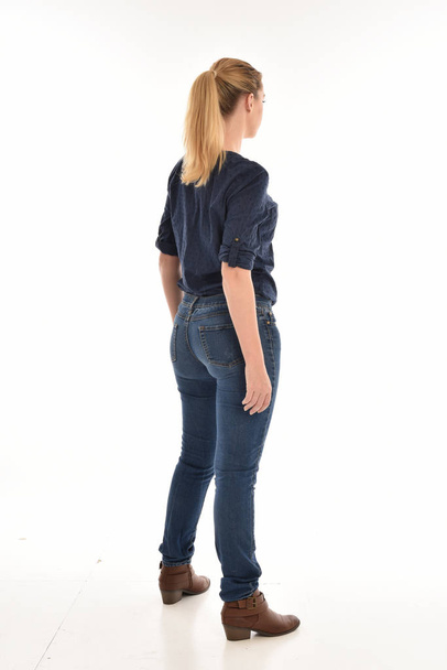 retrato de comprimento total da menina loira vestindo camisa azul simples e jeans, em pé pose de frente para longe da câmera. isolado em fundo branco
. - Foto, Imagem