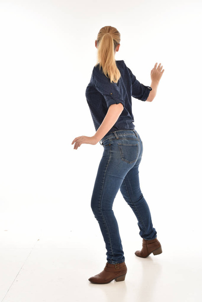 full length portrait of blonde girl wearing simple blue shirt and jeans, standing pose facing away from the camera. isolated on white background. - Photo, image