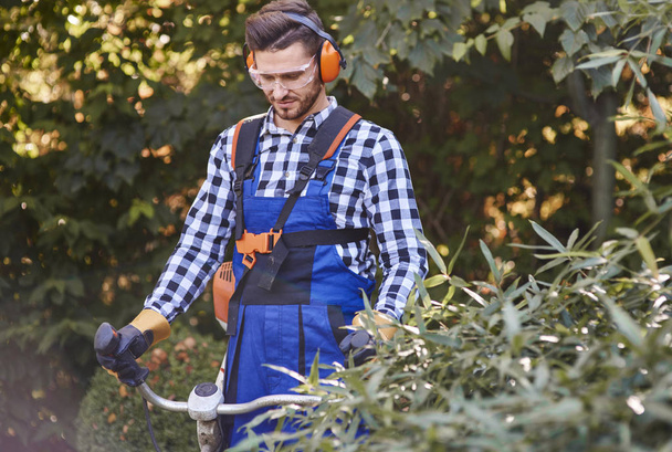 Gardener with goggles and headphones using weedwacker - Φωτογραφία, εικόνα