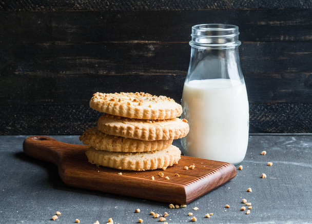 Pilha de biscoitos anel polvilhado com amendoins em uma placa de madeira. Uma garrafa de vidro de leite está perto
. - Foto, Imagem
