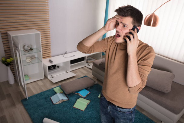 Worried Young Man Talking On Phone About Stolen Television Set At Home - Foto, Imagen