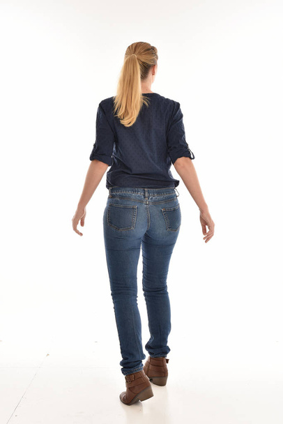 Portret van de volledige lengte van blond meisje dragen van eenvoudige blauw shirt en spijkerbroek, staande pose geconfronteerd weg van de camera. geïsoleerd op witte achtergrond. - Foto, afbeelding