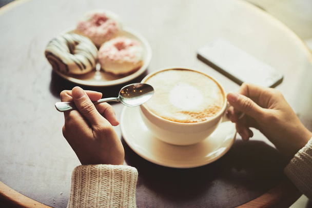 részleges kilátás nyílik a nő élvezi illatos cappuccino és finom fánk asztalnál ülve - Fotó, kép