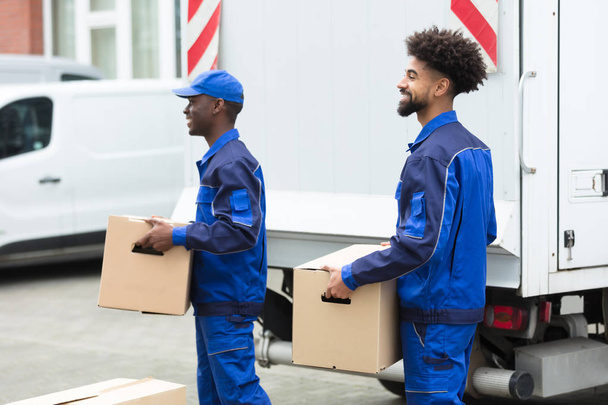 Close-up Of Two Delivery Men Holding The Cardboard Boxes - Fotografie, Obrázek