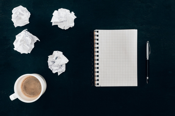 top view of blank notebook with messy crumpled papers and cup of coffee isolated on black - Fotoğraf, Görsel