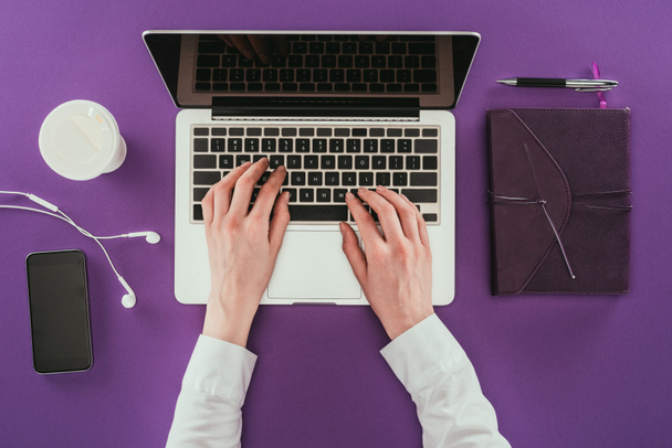 обрізаний знімок бізнес-леді, що працює з ноутбуком на фіолетовій поверхні
 - Фото, зображення
