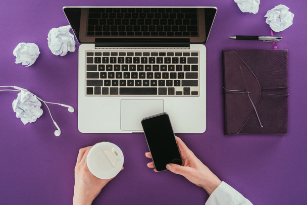 Schnappschuss von Geschäftsfrau mit Smartphone und Kaffeetrinken am Arbeitsplatz auf lila Oberfläche - Foto, Bild