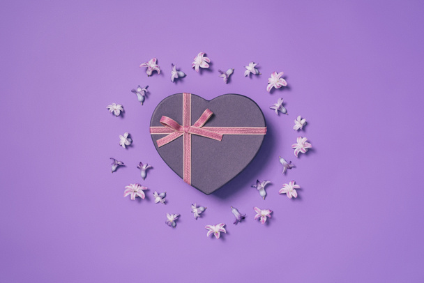 top view of heart shaped gift box with flowers around isolated on purple - Zdjęcie, obraz