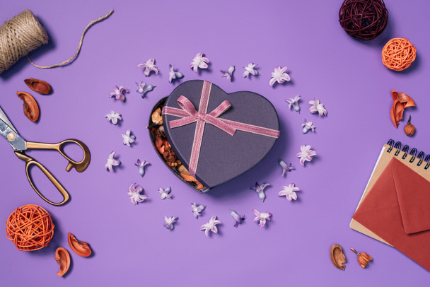 plano con caja de regalo en forma de corazón, flores, tijeras, cuerda y sobre aislado en púrpura
 - Foto, Imagen