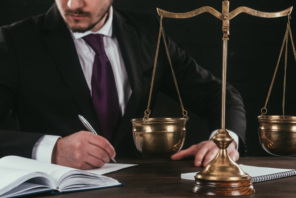 cropped shot of lawyer doing paperwork at workplace with scales isolated on black - Photo, Image