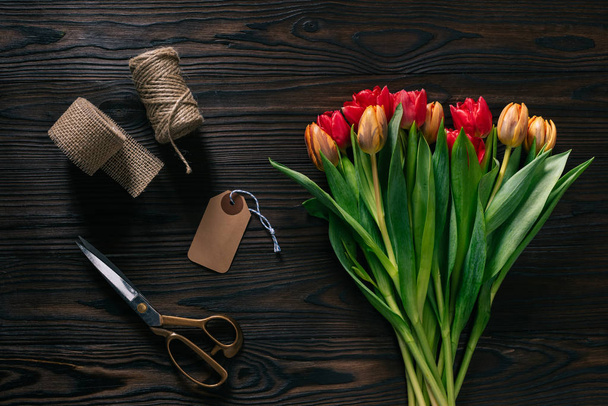 top view of arranged tulips, rope, scissors and ribbon for decoration on wooden surface - Foto, afbeelding