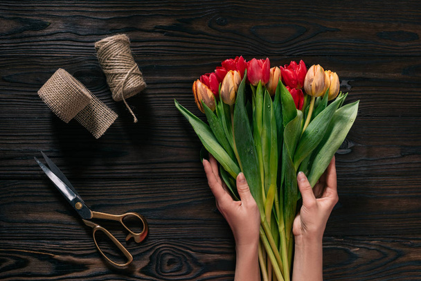 Teilansicht weiblicher Hände, Seil, Schere und Blumenstrauß auf Holzoberfläche - Foto, Bild